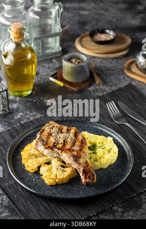 Ready to eat grilled pork chop dinner served with mashed potatoes and roasted cauliflower on a dark plate Stock Photo
