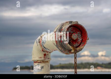Detail of an old pioe on a boat. Beige and peelend of red color. Hanging rusted chain. Island Corfu, Ionian sea and cloudy sky in the background. Corf Stock Photo
