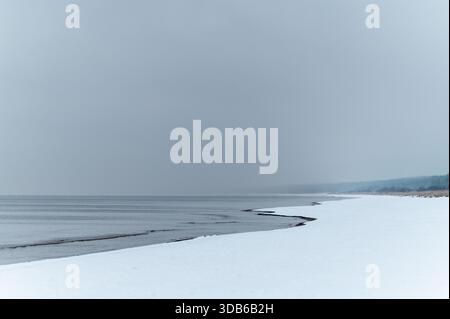 Minimalist winter seascape showing frozen Baltic Sea with natural ice formations creating winding patterns along snowy beach. Stock Photo