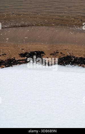 Minimalist natural composition showing transition between white snow-covered sandy beach and brown Baltic Sea water with gentle waves. Stock Photo