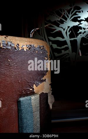 Damaged dark synthetic leather sofa. Old cracked damaged leather on synthetic leather sofa upholstery. Stock Photo