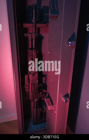 Open tall gun safe containing a modern semi-automatic tactical rifle, illuminated by dramatic red and purple ambient light in a secure residential set Stock Photo