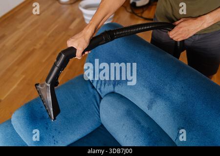 High-angle view of cleaning service worker using washing vacuum cleaner to remove dirt and stains from blue sofa in living room, ensuring clean and Stock Photo