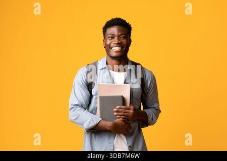 Positive african american guy student with books on yellow Stock Photo