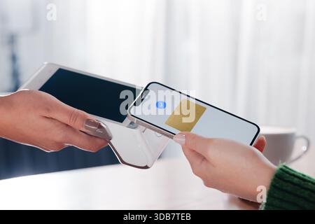 Woman using mobile phone for NFC contactless payment via terminal in cafe, modern digital transaction. Stock Photo