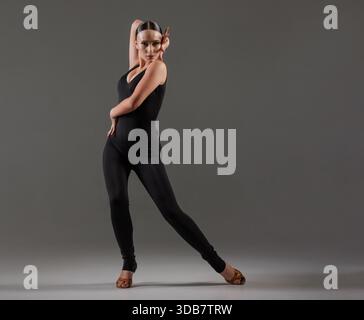 Elegant female dancer in black bodysuit posing gracefully in studio with expressive hand movements and poised stance. Dance concept, lessons, school Stock Photo