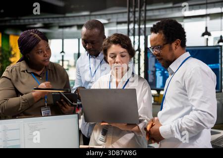 Teamworking programmers brainstorming ways to develop applications in startup office, looking at laptop screen. Engineers optimizing performance by debugging application code to resolve issues Stock Photo