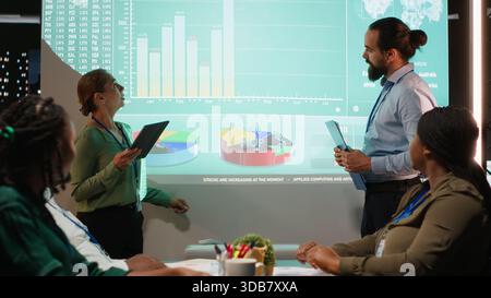 Diverse staff from an enterprise sharing data analytics and insights for a new project agenda during late night corporate meeting. Workers discuss about resources allocation. Camera B. Stock Photo