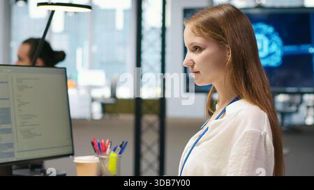 Female technician using AI LLM chatbot to automate tasks in office. IT specialist uses artificial intelligence large language model assistant, optimizing company systems performance, camera A Stock Photo