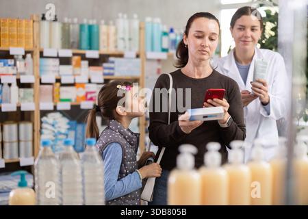 Woman using phone to check ingredients of ointment with pharmacist guidance Stock Photo