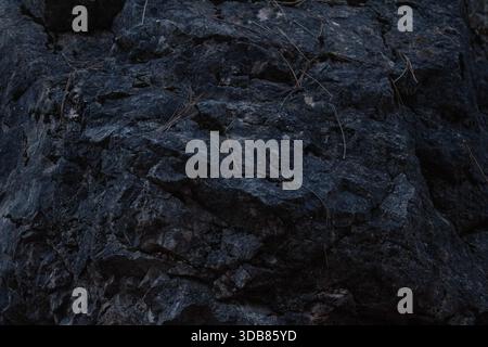 Dark natural stone surface with rough, uneven structure and deep earthy tones, creating a dramatic organic texture suitable for abstract backgrounds, Stock Photo