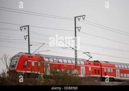 Red double-decker electric train traveling on a railway line under overhead power lines Stock Photo