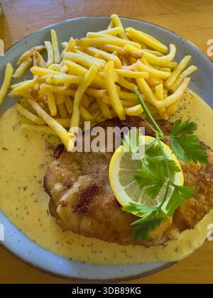 Crispy fried schnitzel served with golden french fries and a rich yellow sauce Stock Photo