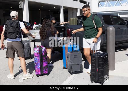 Passengers arrive with rolling luggage at the Norwegian Cruise Line terminal in Miami as vehicles unload travelers at the curb. Stock Photo