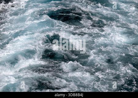 Churning blue ocean wake created by a large ship at sea, with turbulent white foam and swirling water patterns. Stock Photo
