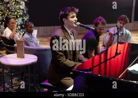 "Performer from The Choir of Man playing the piano during a Q&A session on a cruise ship, with a Christmas tree in the background." Stock Photo