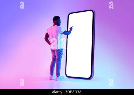 Young Black Man Interacts With Large Smartphone Screen in Neon Lighting for App Design Stock Photo