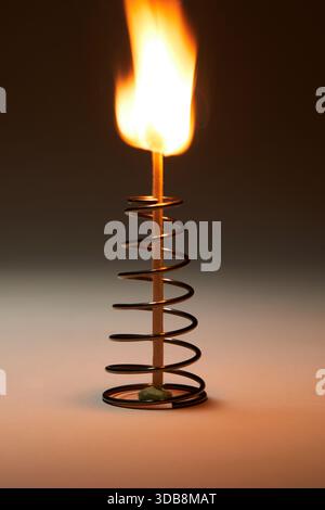 Burning matchstick with flame standing in a metal spring coil holder Stock Photo