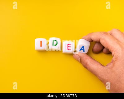 Creative concept of word IDEA formed with colorful blocks arranged by hand on yellow background. Brainstorming, inspiration, learning, and innovative Stock Photo