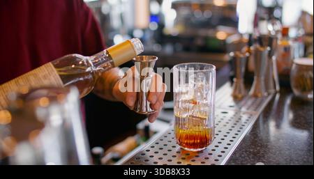 Mixologist work. Making cocktail. Bartender pouring sweet aroma color syrup from metal jigger to glass. Flavored refreshing drink. Stock Photo