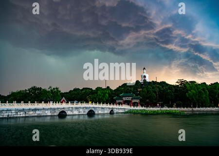 Dark storm clouds gather over Beihai Park in Beijing, at dusk before an approaching thunderstorm, with the White Dagoba and historic bridges. Stock Photo