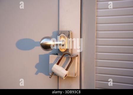 close-up of a metallic door knob with a weathered white padlock on a textured gray door featuring soft sunlight and shadows, evoking themes of securit Stock Photo