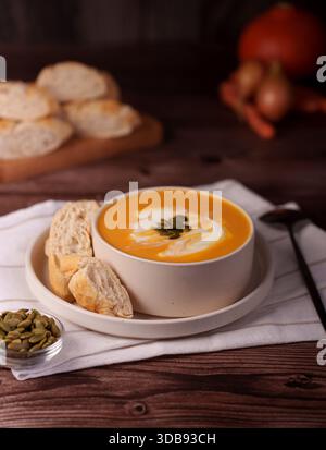 cozy autumn soup scene with vibrant pumpkin soup garnished with seeds, freshly baked bread slices, and warm tones in a rustic wooden kitchen setting, Stock Photo