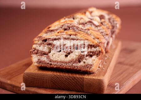 close-up slice of marbled cocoa and vanilla loaf cake on wooden board with warm brown background highlighting textured patterns and rustic presentatio Stock Photo