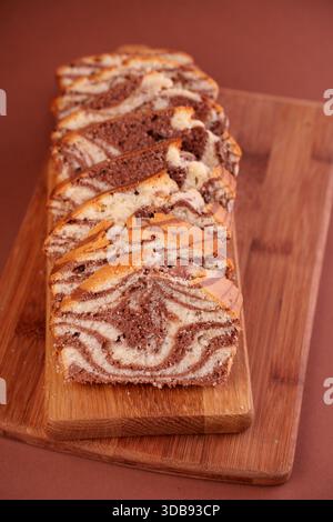 sliced marble cake on wooden cutting board with rich chocolate and vanilla swirls against a warm brown background creating an appealing contrast of co Stock Photo