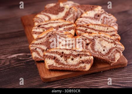 sliced marble cake with chocolate and vanilla swirls on wooden board against dark wooden background, highlighting texture and contrast in a cozy, rust Stock Photo