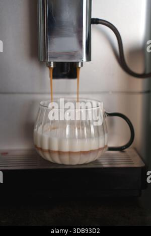 close-up of espresso machine pouring layers of espresso into a clear glass cup with milk, creating a visually appealing layered coffee drink in a mode Stock Photo