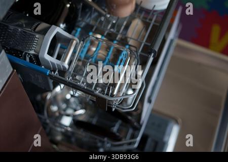 close-up view of a kitchen dishwasher mid-cycle showcasing various kitchen utensils and glassware neatly arranged on metal racks with an emphasis on d Stock Photo