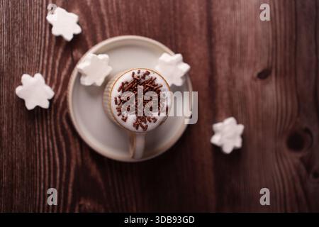 overhead view of cappuccino with chocolate sprinkles surrounded by decorative marshmallows on a rustic wooden table setting, contrast, homey, serenity Stock Photo