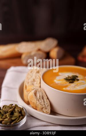 warm autumnal setting with creamy pumpkin soup, artisan bread, and toasted pumpkin seeds on a rustic wooden table, prepared, elegant, appetite, savory Stock Photo