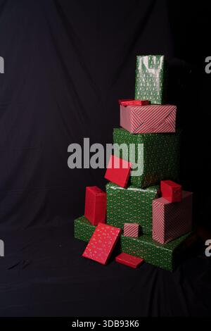 stack of multiple red and green christmas presents against a dark fabric backdrop, showcasing a festive yet minimalist holiday theme with various size Stock Photo