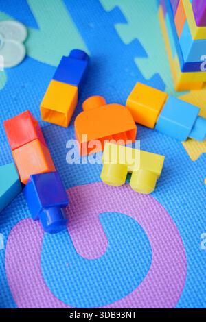 colorful plastic building blocks scattered on a textured blue mat with pink, yellow, and green accents, showcasing a vibrant and playful arrangement c Stock Photo