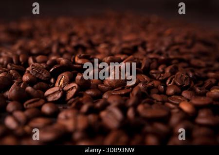 close-up view of rich brown coffee beans spread across a dark surface, highlighting their textured surface and deep earthy tones in a warm, inviting a Stock Photo
