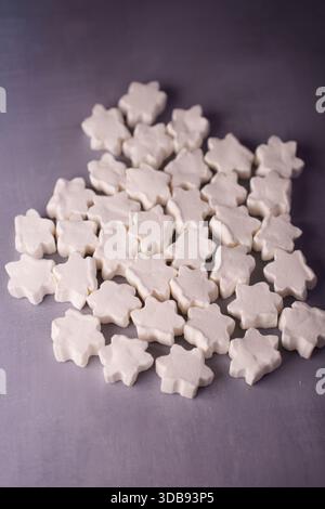 cluster of star-shaped white candies arranged randomly on smooth gray surface creating a clean and minimalistic look with soft textures and subtle lig Stock Photo