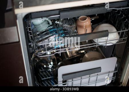 open dishwasher loaded with an assortment of dishes, glasses, and utensils, displaying a blend of materials and muted colors in a home kitchen setting Stock Photo