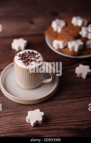 a cozy coffee cup topped with chocolate shavings sits beside a plate of star-shaped cookies, creating a warm and inviting setting on a rich wooden sur Stock Photo