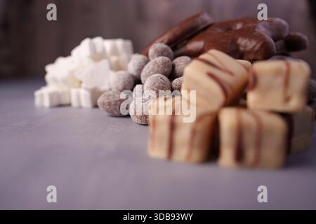 a close-up of assorted sweets: chocolate-covered treats, white marshmallows, and cocoa-dusted truffles displayed on a matte grey surface in a warm, so Stock Photo