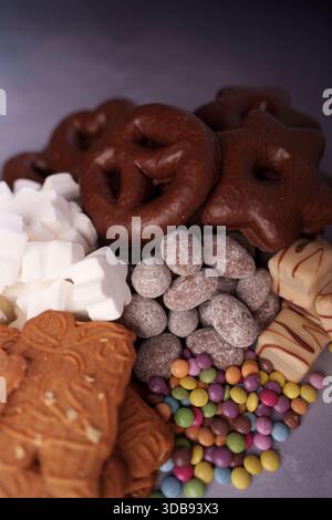 assorted sweets and treats including chocolate pretzels, sugar-coated nuts, colorful candy, white marshmallows, and decorated cookies on a textured su Stock Photo