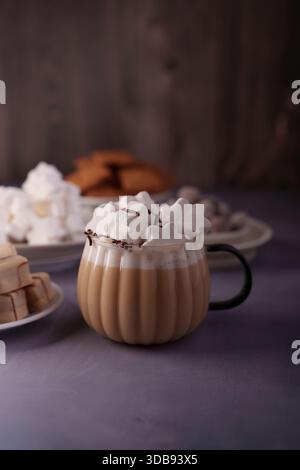 cozy hot chocolate with star-shaped marshmallows in a textured mug surrounded by assorted confections on a soft grey surface and a warm wooden backgro Stock Photo