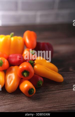 vibrant array of assorted peppers on wooden table with soft brick wall backdrop, showcasing a colorful and fresh presentation of yellow, orange, and r Stock Photo