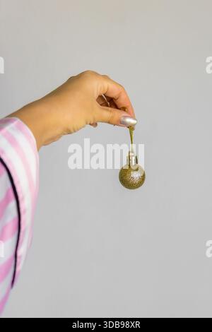 Female hand holding golden Christmas bauble on neutral background. Stock Photo
