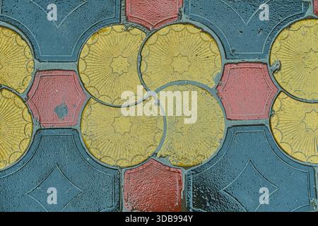 Wet geometric tile pattern on urban pavement after rain. Decorative stone surface with repeating mosaic design, suitable for abstract background, Stock Photo