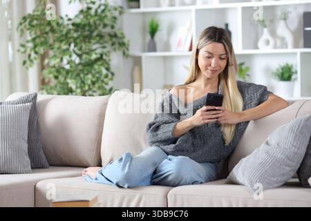 Relaxed woman using cell phone sitting on a couch at home Stock Photo