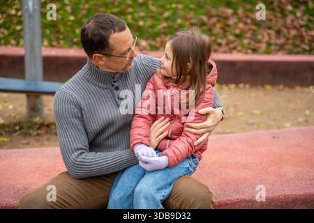 Father and daughter sitting close and talking on the playground border. Tender moment of connection and support. Stock Photo