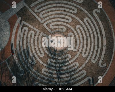 Aerial view of an intricate circular labyrinth pattern etched into the earth, a blend of light stone and dark soil creating a mesmerizing contrast, Bo Stock Photo