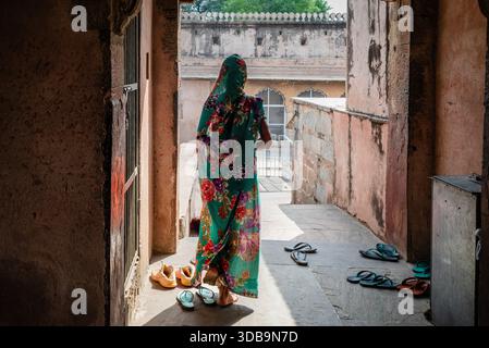 Woman in a floral sari standing in a narrow corridor with sandals on the floor, inside a historic building in India. Stock Photo